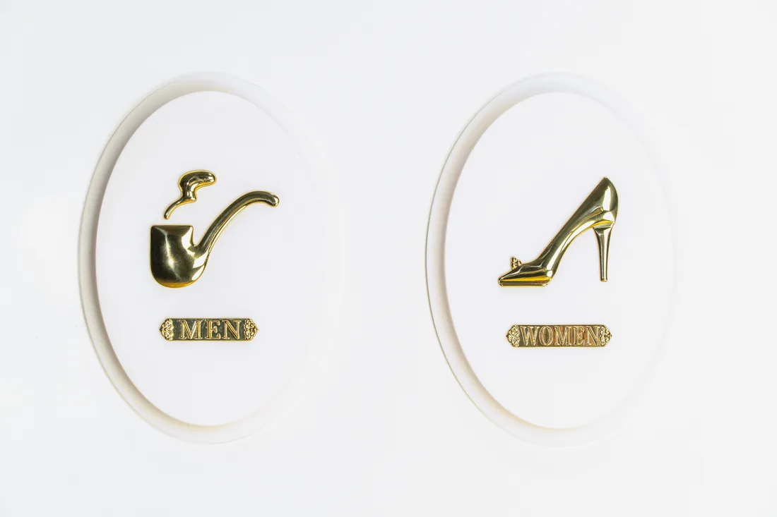 White oval restroom plaques with gold pipe and high-heel icons