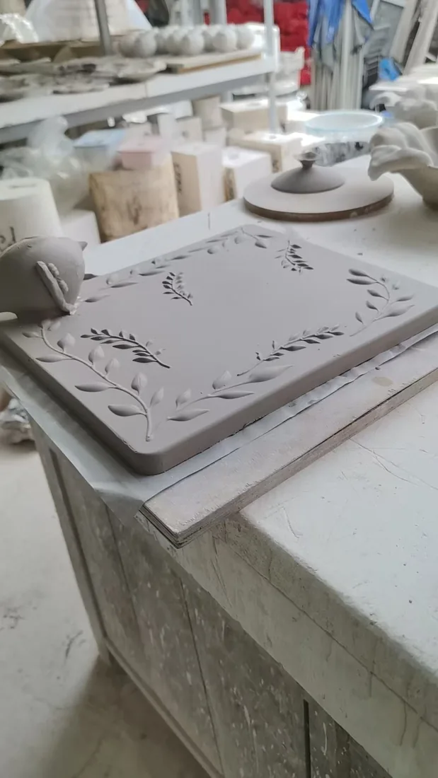 Unfired clay plaque with carved leaf border on the pottery workbench
