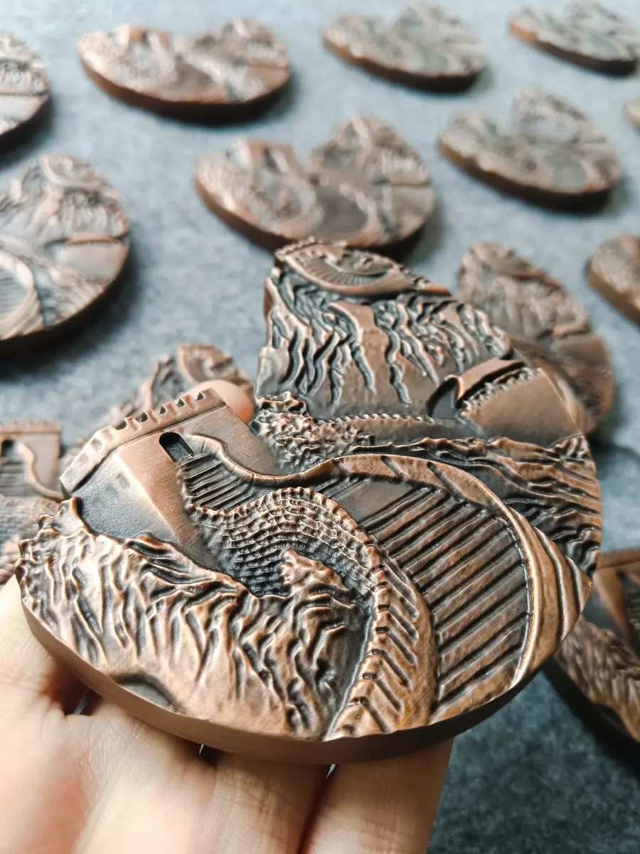 Real aluminum fish relief samples with copper-colored raised details and dark recessed textures, with one sample held in a hand